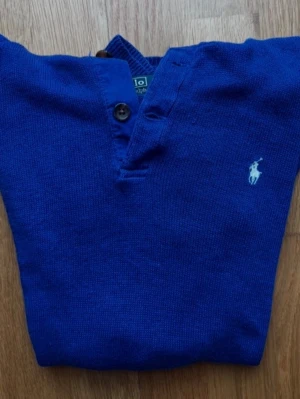 Blå stickad tröja från Ralph Lauren - Klassisk blå stickad tröja från Ralph Lauren med  två encompassing knappar. Tröjan har det ikoniska vita loggan på bröstet. Storleken är 14-16 och össsar dig som är 165. Priset är ej hugget i sten. Hör av dig vid minsta fråga!