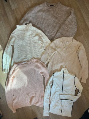 Långärmad tröja  - Ett paket med fem stickade/virkade tröjor. Två av dem är tjocktröjor. Den beige längst upp är i storlek XL (Gina tricot). Den vita under till vänster är i storlek 36/38 från Kappahl. Bredvid är den i storlek XS från Cubus men passar en S/M också. Den persikofärgade är i storlek M från Noisy May. Den vita med svart streck är i storlek S från Zara.