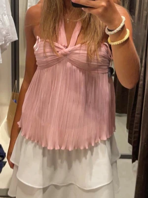 Ljusrosa plisserad halterneck topp - Säljer en ljusrosa plisserad halterneck topp med twistad detalj framtill. Toppen är ärmlös och har en luftig, flowy passform som ger en söt och trendig look. 