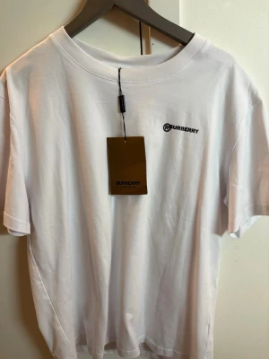 Vit Burberry t-shirt med tryck - Vit t-shirt från Burberry med svart logga på bröstet och ett stort statement-tryck på ryggen: 'Don't believe everything you think'. Klassisk rund hals och korta ärmar. Tillverkad i mjuk bomull för en skön och avslappnad look.