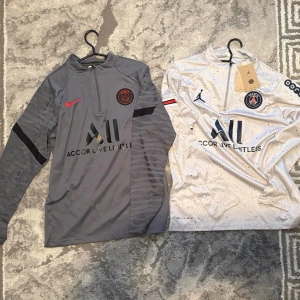 PSG långärmad träningströja Nike - Säljer två långärmade träningströjor från Paris Saint-Germain ⚽️🔥  1. Grå tröja • Svarta och röda detaljer • PSG-logga • Nike märke • Snygg och sportig design  2. Vit tröja • Svarta och röda detaljer • PSG-logga • Jordan märke • Ooredoo-tryck på ärmen • “Accor Live Limitless” sponsor  • Båda är långärmade träningströjor • Bekväma och perfekta till träning eller vardag • Fint skick  📦 Skickas samma dag vid snabb affär Först till kvarn 🔥