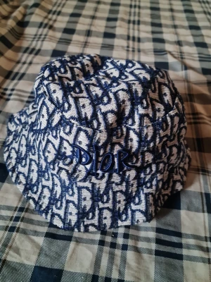 Reversibel bucket hat från Dior - Snygg bucket hat från Dior som är vändbar. Ena sidan är helsvart med vit broderad Dior-logga, andra sidan har blått och vitt mönster med blå Dior-broderi. Perfekt accessoar för att lyfta din stil. Tillverkad i tyg med mjuk känsla.