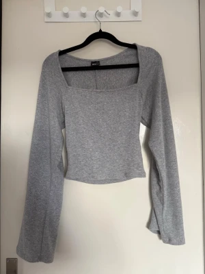 Grå långärmad croppad topp - Snygg grå croppad topp med lång ärm och fyrkantig ringning. Tillverkad i mjukt bomullsmaterial som känns skönt mot huden. Perfekt för en trendig och avslappnad look.