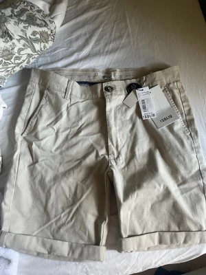 Beige shorts från Solid  - Snygga beige shorts från Solid med klassisk design, uppvikta benslut och sidofickor. Baktill finns två fickor med knappstängning. Perfekta för varma dagar och lätta att matcha med olika outfits.