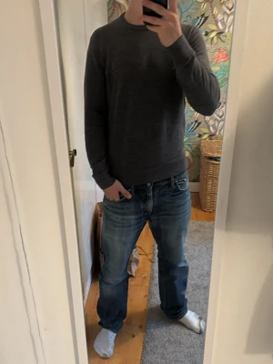 Mörkgrå stickad tröja från Uniqlo - Säljer en stilren mörkgrå stickad tröja från Uniqlo. Tröjan har rund halsringning och långa ärmar, perfekt för lager-på-lager. Enkel design som passar till det mesta och är gjord i mjukt material för extra komfort.