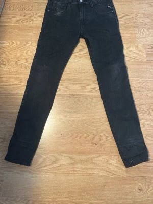 Svarta slim fit jeans från Replay - Säljer ett par svarta slim fit jeans från Replay med klassisk femficksmodell och låg midja. Jeansen har smal passform och är tillverkade i stretchigt material för extra komfort. Perfekta för en trendig och avslappnad stil.