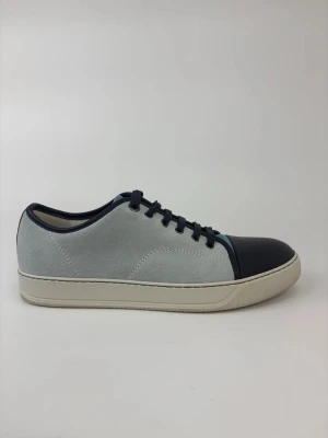Gråblå Lanvin sneakers med mockadetaljer - Snygga sneakers i ljusgrå mocka med mörkblå tå och detaljer. Skorna har vita sulor och mörkblå snörning som ger en clean och modern look. Perfekta för dig som gillar stilrena och minimalistiska sneakers.
