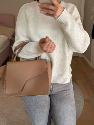 Beige handväska med axelrem från ATP atelier - Snygg beige handväska från ATP atelier i slätt konstläder med både handtag och justerbar axelrem. Väskan har en stilren, fyrkantig form och lock med mjukt rundad kant. Perfekt för dig som gillar minimalistisk och modern design. Väskan köptes för några år sedan och har använts fåtal gånger. Finns lite repor på framsidan men inget som syns mycket. 