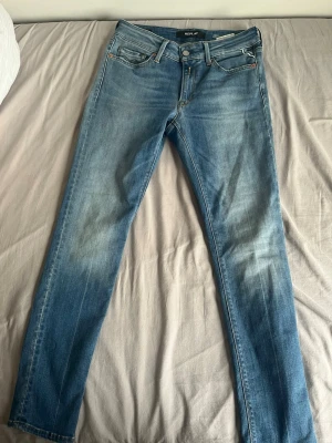 Blå slim fit jeans från Replay - Snygga blå slim fit jeans från Replay med klassisk femficksdesign och lätt slitna detaljer framtill. Jeansen har normal midja, dragkedjegylf och är tillverkade i stretchigt denim för extra komfort.