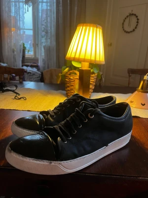LANVIN CAPTOE - Snygga svarta sneakers med klassisk vit sula och svarta skosnören. Skorna har en låg profil och rundad tå, vilket ger en clean och stilren look. Perfekta för dig som gillar enkel och tidlös design.
