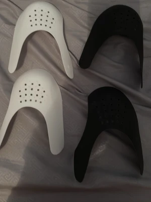 Svarta och vita skoinlägg för tåbox / crease skydd  - Fyra skoinlägg i plast, två svarta och två vita, designade för att placeras i tåboxen på sneakers för att behålla formen. Inläggen har perforerade hål för ventilation och är formade för att passa de flesta sneakers. Crease skydd, vita i storlek S och svarta i storlek L. Säljer båda.