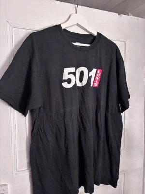 Svart Levi's 501 t-shirt vintage fit - Svart t-shirt från Levi's med vintage fit och stort vitt 501-tryck samt röd Levi's-logga på bröstet. Klassisk rund hals och korta ärmar. Tillverkad i bomull, perfekt för en avslappnad och cool stil.