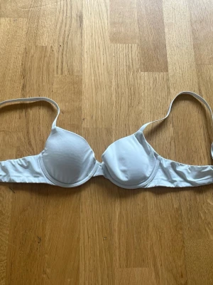 Vit bygel-bh med vadderade kupor - Säljer en klassisk vit bh med bygel och vadderade kupor. Bh:n har justerbara axelband och slät design utan spets eller mönster. Perfekt för dig som vill ha en enkel och stilren bh under alla typer av kläder.