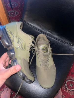 Nike Air Vapormax olivgröna sneakers - Nike Air Vapormax sneakers i olivgrönt med genomskinlig sula och kamouflagemönster på plösen och sidan. Snygg design med mesh och syntetmaterial, samt klassisk Nike-logga på sidan. Perfekta för dig som gillar streetwear och sportig stil. 