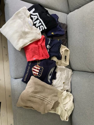 Stort klädpaket med tröjor & t-shirts - Säljer ett klädpaket med flera tröjor och t-shirts i olika färger och stilar. Innehåller bland annat svart Vans t-shirt, beige och vita stickade tröjor, marinblå Gant t-shirt, röd t-shirt samt plagg från Sail Racing och Lyle & Scott. Perfekt för dig som vill uppdatera garderoben!
