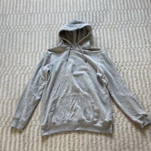 Grå hoodie med huva - En stilren ljusgrå hoodie från lager 157 i storlek M. Tröjan har klassisk huva med snörning, magficka och ribbade muddar. 