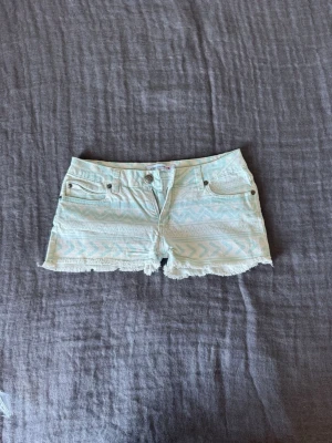 Mintgröna mönstrade shorts från Fishbone - Snygga mintgröna shorts från Fishbone med ljusa etnomönster och råa kanter. Klassisk femficksmodell med dragkedja och knapp framtill. Perfekta för varma dagar och en avslappnad stil.