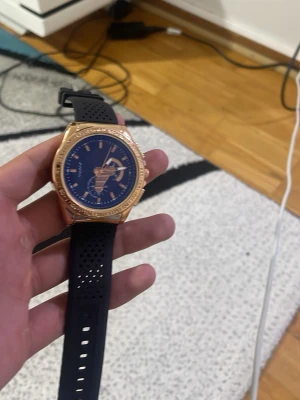 Svart och guld klocka från Guess - Stilren klocka från Guess med svart silikonarmband och blå urtavla. Boetten är i guldtonad metall och har markerade detaljer runt urtavlan. Perfekt accessoar för dig som vill ha en sportig men ändå elegant look.