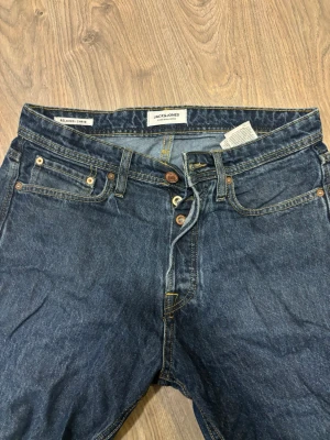 Mörkblå relaxed jeans Jack & Jones - Snygga mörkblå jeans från Jack & Jones i relaxed fit. Klassisk femficksmodell med knäppning fram och kontrastsömmar. Perfekta för en avslappnad stil och tillverkade i slitstarkt denimtyg.