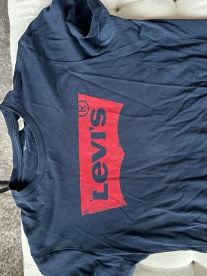 Blå Levi's t-shirt med röd logga - Snygg blå t-shirt från Levi's med den klassiska röda loggan tryckt framtill. T-shirten har rund halsringning och korta ärmar, perfekt för en avslappnad och trendig stil.