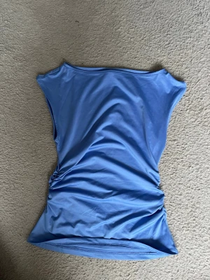 Blå ärmlös topp i stretchigt material - TRYCK EJ KÖP DIREKT!!💗Snygg blå topp med ärmlös design och lätt figurnära passform. Tillverkad i ett stretchigt syntetmaterial som ger en smickrande siluett. Perfekt att styla med jeans eller kjol för en trendig look. Hör av dig vid intresse💗