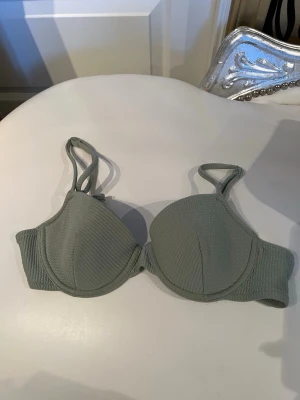 Ljusgrön bikiniöverdel från H&M - Trendig ljusgrön bikiniöverdel från H&M med vadderade kupor och dubbla axelband. Materialet har en ribbad struktur som ger en snygg och modern känsla. Perfekt för stranddagar och poolhäng.