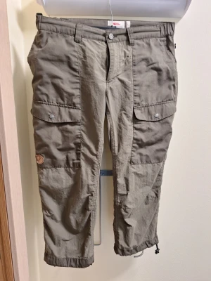 Fjällräven Abisko Hybrid Knickers - Snygga knickers från Fjällräven med stora fickor på sidorna och justerbara benslut med dragsko. Byxorna har klassisk cargomodell och är tillverkade i slitstarkt material, snabbtorkande, lätta och perfekta för äventyr och vardag. Ikonisk Fjällräven-logga på benet.
