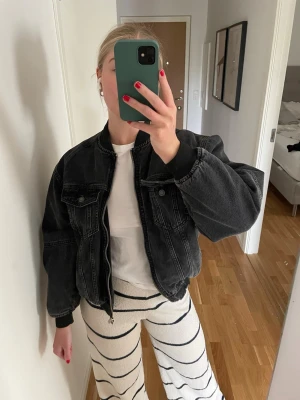 Svart oversized bomber jeansjacka - Cool svart jeansjacka i oversized modell med breda axlar och muddar vid ärmslut. Jackan har två bröstfickor med lock och knappar samt dragkedja framtill. Använd ett fåtal gånger. Nypris var runt 700 kr 