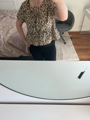 Leopardmönstrad blus med knyt - Snygg blus med leopardmönster och korta ärmar. Modellen har en lös passform och knytning framtill vid halsen. Materialet känns lätt och luftigt.