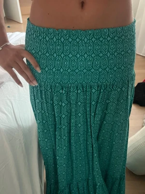 Grön långkjol med grafiskt mönster zara trend - Säljer en grön långkjol med grafiskt mönster. Kjolen har bred resår i midjan och ett flowy fall som ger en avslappnad vibe. Perfekt till sommaren och enkel att styla med crop tops eller linnen.