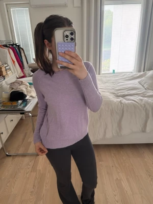 Ljuslila stickad tröja - Säljer en ljuslila stickad tröja med rund halsringning och långa ärmar. Tröjan har ribbstickade muddar vid ärmslut och nederkant, vilket ger en snygg och enkel look. Perfekt att matcha med jeans eller kjol för en avslappnad stil.