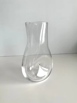 ”Nipple” - handblåst karaff i glas av Sara Mannheimer  - Stilren handblåst kanna / karaff ”Nipple” av fantastiska erkända glaskonstnären Sara Mannheimer. Cool modell i transparent glas med rundad form och och indrag på sidan samt praktisk pip för enkel upphällning. Perfekt både som karaff för vatten och juice eller som dekantör för vin. Höjd 18 cm. Signerad S. Mannheimer 2001 i botten. Mycket fint skick! 