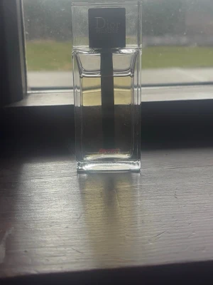 Dior Homme Sport parfym - Dior Homme Sport parfym i en stilren, rektangulär glasflaska med svart fyrkantigt lock. Flaskan är transparent och visar den ljusgula vätskan inuti. Modern och elegant design som passar perfekt i badrumshyllan. 75ml ungefär 50ml kvar