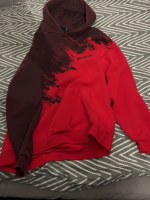 Röd och brun Paranoid hoodie - Säljer en snygg hoodie från Paranoid i rött och brunt med svart grafiskt tryck över bröstet och texten 'Paranoid'. Hoodien har en stor huva och magficka, samt ribbade muddar. Perfekt för dig som vill sticka ut med en unik streetwear-look.