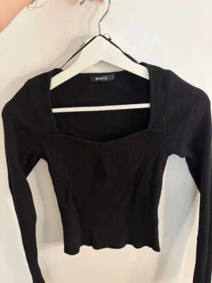 Svart ribbad topp från Ginatricot - Svart ribbad topp från Ginatricot med lång ärm och fyrkantig urringning. Toppen har en figurnära passform. 
