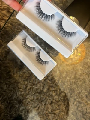 Svarta volymfransar i plast - Två par lösögonfransar i svart med fyllig volym och mjuk, böjd form. Fransarna kommer i vita plastaskar och har en naturlig men dramatisk look. Perfekta för att framhäva ögonen och skapa en intensiv blick.