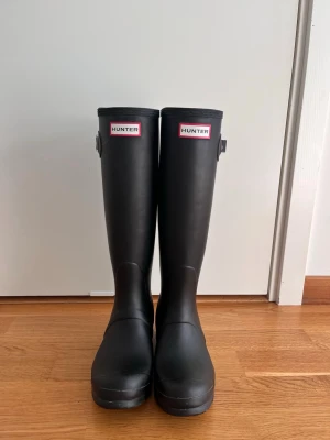 Svarta höga gummistövlar Hunter - Svarta höga gummistövlar från Hunter med logga framtill. Använda endast ett fåtal gånger. Skriv för fler bilder! 