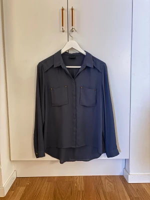 Mörkgrå blus med fickor - Stilren mörkgrå blus med två bröstfickor och guldfärgade knappar. 