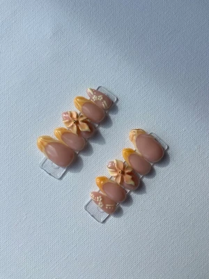 Press-on naglar med blommor och gult - Snygga press-on naglar i oval form med nude bas och detaljer i gult och vitt. Några naglar har 3D-blommor och små pärlor för extra wow-effekt. Perfekt för dig som vill ha en unik och trendig look. Materialet är plast l gel