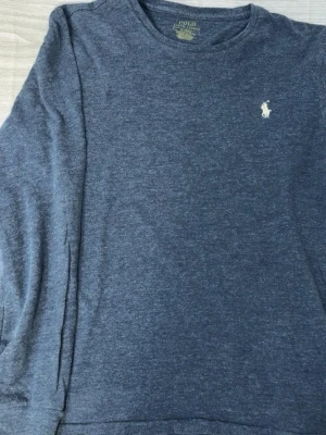 Mörkblå tröja från Polo Ralph Lauren - Mörkblå långärmad tröja från Polo Ralph Lauren i custom slim fit. Tröjan har rund halsringning och den klassiska broderade loggan i vitt på bröstet. Perfekt för en clean och stilren look.