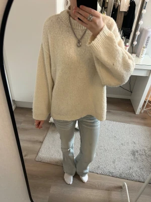 Oversized cremevit stickad tröja - Mysig oversized stickad tröja i cremevitt med rund hals och breda ärmar. Tröjan har en enkel, stilren design och är gjord i ett mjukt, fluffigt material som passar perfekt för kalla dagar.