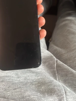 Svart smartphone med glasfront - Säljer en svart smartphone med stor skärm och rundade hörn. Telefonen har en modern design med glasfront och metallram. Perfekt för dig som gillar stilrena mobiler och vill ha en enkel, snygg look.