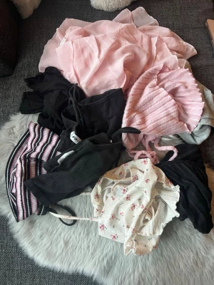 Mix av toppar i olika färger och stilar - Säljer ett paket med flera olika toppar i blandade färger och material. Innehåller bland annat en rosa ribbad topp, svart linnetopp, vit blommig topp med volangdetaljer och en randig topp i rosa, svart och vitt. Perfekt för dig som vill uppdatera garderoben med olika stilar. 9 st från new yorker och shein storlek xxs-s