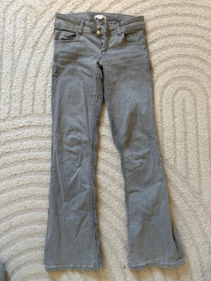 Grå bootcut jeans med dubbla knappar - Snygga grå jeans med bootcut passform och dubbla knappar i midjan. Klassisk femficksmodell och bälteshällor. Perfekta för dig som gillar en lite vidare siluett nertill. Materialet är mjukt och stretchigt för extra komfort. Storlek 158, men jag som har storlek S använder. 