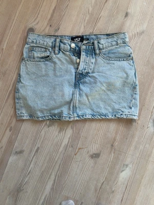 Ljusblå jeanskjol från 157 - Säljer en ljusblå jeanskjol från 157 med klassisk femficksdesign och dubbla knappar framtill. Kjolen har en kort passform och är tillverkad i denim, perfekt för dig som gillar en enkel och tidlös stil. XXS men passar mig som har XS/S med tajt passform. 