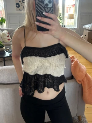 Stickad svartvit topp - Snygg linnetopp med tunna axelband i svart. Toppen är stickad med volangdetaljer och har en vågig kant nertill. Den svarta färger har lite skimmer i sig. Använts 1 gång. 