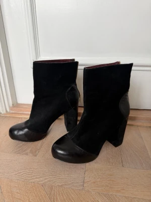 Svarta stövletter i mocka och läder - Säljer ett par svarta stövletter med chunky klack och rund tå. Skorna är i en mix av mocka och slätt läder, med dragkedja på sidan för enkel påtagning. 