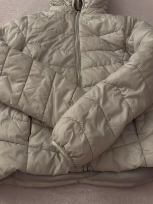 Ljusbeige pufferjacka med dragkedja - Säljer en ljusbeige pufferjacka med hög krage och hel dragkedja framtill. Jackan har quiltade sömmar och en klassisk puffig look. Perfekt för kalla dagar och riktigt skön att bära. Passar dig som gillar enkel och stilren design.
