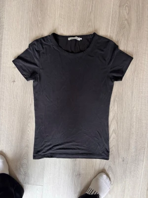 Svart t-shirt från Samsøe Samsøe - En enkel och stilren svart t-shirt från Samsøe Samsøe. T-shirten har rund halsringning och korta ärmar, perfekt för en clean look. Materialet är mjukt och känns som bomull, vilket gör den skön att bära hela dagen.