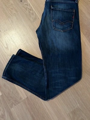 Replay Anbass - Snygga mörkblå jeans med raka ben och kontrastsömmar. Jeansen har klassisk femficksmodell och coola slitningar framtill. Skicket är mycket bra, modellen är anbass och storlek är W30 L32.                       Ytterbenslängd:97 Innerbenslängd:73 Midjan:39 sida till sida